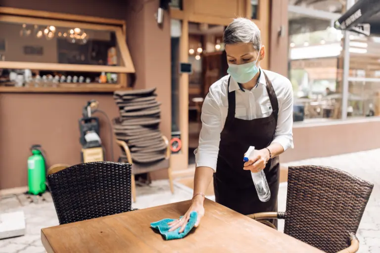 une serveuse de restaurant portant un masque pendant qu'elle nettoie la surface d'une table