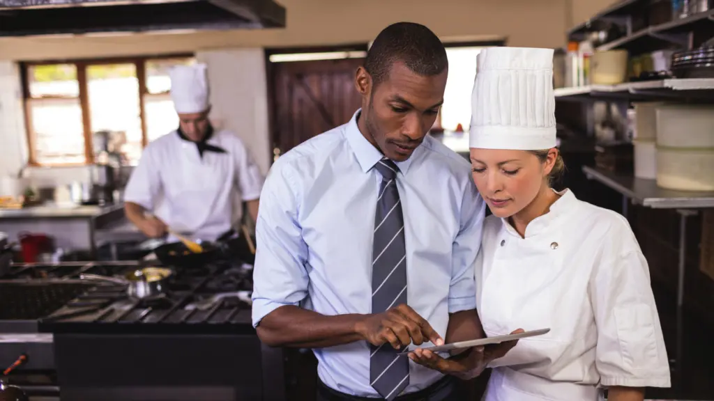 Personnel de restauration collective : un manager montre au cuisinier quelque chose sur l'écran d'une tablette.