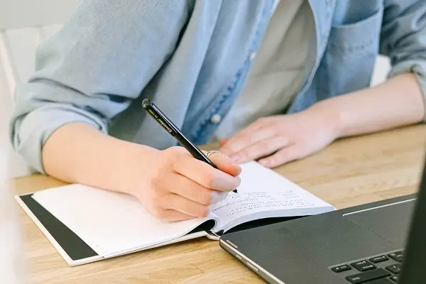 Une personne assise prenant des notes sur une table devant son ordinateur